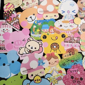 May include: A collection of colorful, cartoon-themed paper cutouts with various designs, including mushrooms, a donut, a skull, a frog, and a bear. The cutouts are decorated with glitter, polka dots, and other embellishments. The text "mushroom", "sweet", "Rilakk", "くじ運", and "ラブラブ" is visible on some of the cutouts.