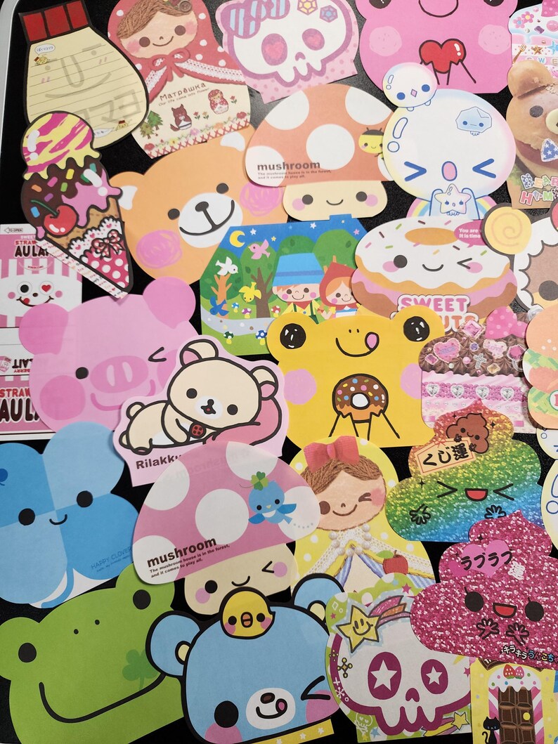May include: A collection of colorful, cartoon-themed paper cutouts with various designs, including mushrooms, a donut, a skull, a frog, and a bear. The cutouts are decorated with glitter, polka dots, and other embellishments. The text "mushroom", "sweet", "Rilakk", "くじ運", and "ラブラブ" is visible on some of the cutouts.