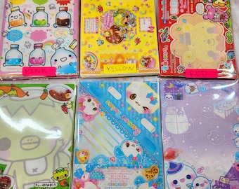 May include: Six colourful paper packs with different designs. The packs are labelled with the colours pink, yellow, red, green, blue, and purple/fuchsia. Each pack features a different cartoon character or design.