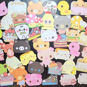 May include: A collection of colorful, die-cut sticky notes in various shapes, including animals, food, and other cute designs. The notes feature illustrations of pigs, bears, cats, cakes, and ice cream. Some notes have text, such as "Baby Infinite" and "Happy Sweet".