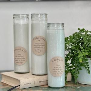 Puede incluir: Tres tarros de velas de vidrio blanco con etiquetas de papel marrón que contienen versículos bíblicos. Las etiquetas incluyen los versículos Jeremías 42:3, Salmo 90:14 e Isaías 55:3.