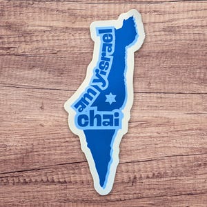 May include: A blue sticker in the shape of Israel with the words "am yisrael chai" in blue text. A Star of David is in the center. The sticker is on a wooden surface.