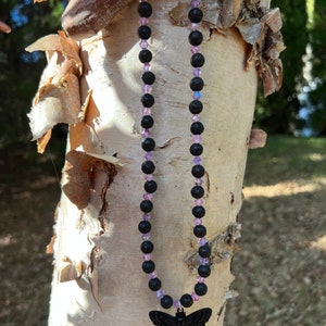 Puede incluir: Un collar de cuentas de lava negra y cristal morado con un colgante de polilla negra.