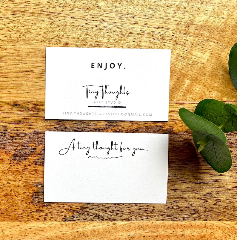 Puede incluir: Tarjeta blanca con texto negro que dice "ENJOY." Debajo del texto est&aacute; el logotipo "Tiny Thoughts Gift Studio" con la direcci&oacute;n de correo electr&oacute;nico "tinythoughts.giftstudio@gmail.com". Una segunda tarjeta blanca con texto negro dice "A tiny thought for you..." con una l&iacute;nea ondulada debajo.