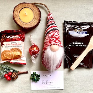 Puede incluir: Una cesta de regalo navide&ntilde;a con un gnomo, una cuchara de madera, una caja de galletas de mantequilla, una trufa de chocolate, una caja de mezcla de chocolate caliente, una vela peque&ntilde;a y una rama de pino.