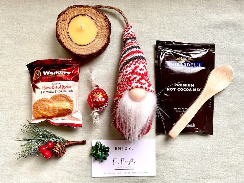 Puede incluir: Una cesta de regalo navide&ntilde;a con un gnomo, una cuchara de madera, una caja de galletas de mantequilla, una trufa de chocolate, una caja de mezcla de chocolate caliente, una vela peque&ntilde;a y una rama de pino.