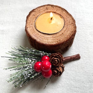 Puede incluir: Un portavelas de madera con una vela de t&eacute; encendida. El portavelas est&aacute; decorado con una rama de pino verde con bayas rojas y pi&ntilde;as marrones.