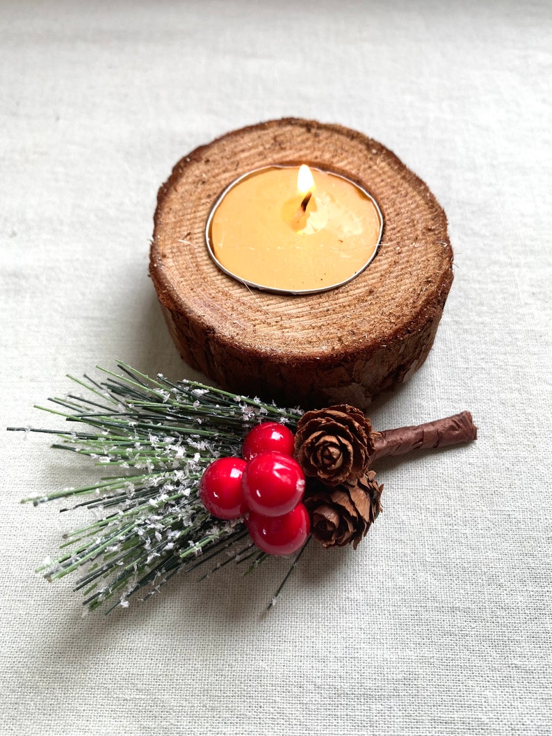 Puede incluir: Un portavelas de madera con una vela de t&eacute; encendida. El portavelas est&aacute; decorado con una rama de pino verde con bayas rojas y pi&ntilde;as marrones.