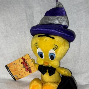 Puede incluir: Peluche de Tweety Bird con un sombrero morado y plateado con una pajarita negra y sosteniendo una bolsa negra. La etiqueta dice "Millennium Looney Tunes 2000" y "Tweety Bean Bag".