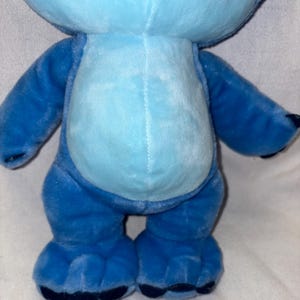 Pu&ograve; includere: Un peluche blu di un personaggio alieno con grandi orecchie, pancia azzurra e artigli blu scuro. Il giocattolo ha un'espressione amichevole ed &egrave; in piedi. Il giocattolo &egrave; un personaggio popolare di un film d'animazione Disney.