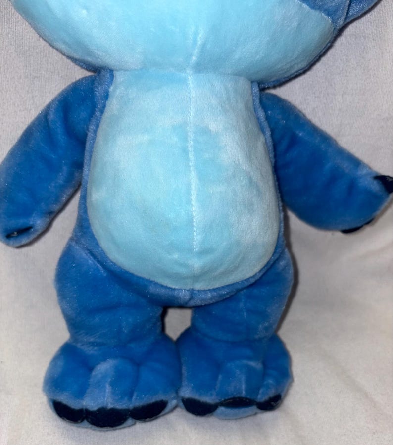 Pu&ograve; includere: Un peluche blu di un personaggio alieno con grandi orecchie, pancia azzurra e artigli blu scuro. Il giocattolo ha un'espressione amichevole ed &egrave; in piedi. Il giocattolo &egrave; un personaggio popolare di un film d'animazione Disney.