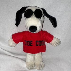 May include: White plush dog wearing black sunglasses and a red shirt with the text "JOE COOL" in black.