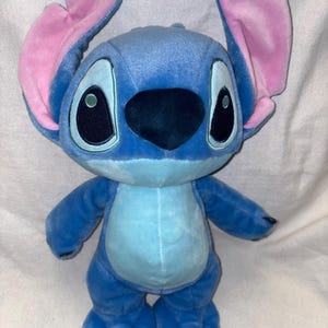 Pu&ograve; includere: Un peluche di Stitch blu con grandi occhi e orecchie rosa. Il peluche ha una pancia azzurra e sta in piedi. Il giocattolo &egrave; basato sul personaggio del film d'animazione, con i suoi quattro arti e le sue caratteristiche distintive.