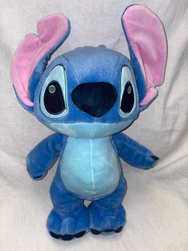 Pu&ograve; includere: Un peluche di Stitch blu con grandi occhi e orecchie rosa. Il peluche ha una pancia azzurra e sta in piedi. Il giocattolo &egrave; basato sul personaggio del film d'animazione, con i suoi quattro arti e le sue caratteristiche distintive.