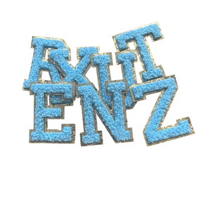 May include: A collection of light blue, fuzzy varsity letters with gold trim. The letters are arranged in a slightly overlapping pattern against a white background. The letters appear to spell out a word or name.