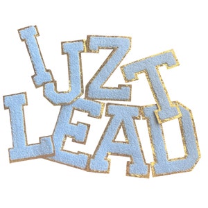 May include: Light blue felt letters spelling out "I Just Lead" with gold glitter outlining each letter.