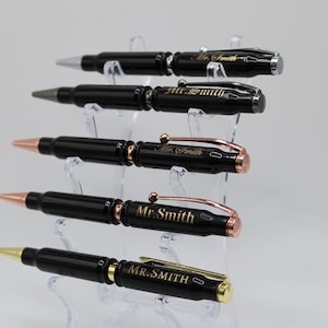 May include: Five black bullet pen style pens with gold lettering on a clear stand. The pens are engraved with the name "Mr. Smith".