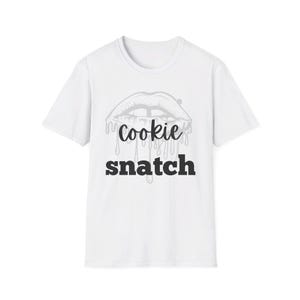 May include: White t-shirt featuring a graphic of lips with dripping detail and the words "cookie snatch" in a bold, black font. The design is centered on the front of the short-sleeved shirt.