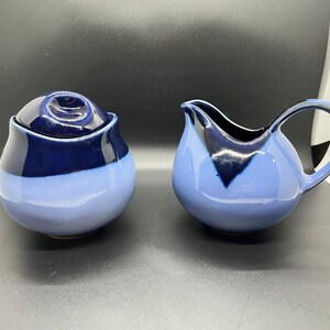 May include: A blue and black ceramic sugar bowl and creamer set. The sugar bowl has a lid and the creamer has a handle.