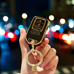 May include: A gold and black car key with a diamond-encrusted keychain. The key has several buttons, including "Hold" and a car icon.
