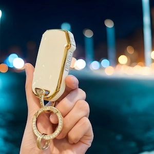 May include: A white and gold car key with a diamond-encrusted key ring. The key has three buttons and the text "RIKEY" is visible on the side.