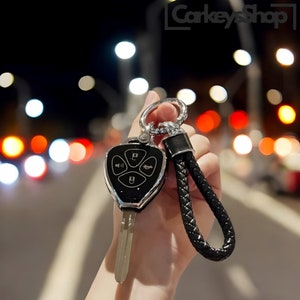 May include: A black car key fob with four buttons, including lock, unlock, trunk, and panic. The key fob is attached to a black leather keychain with a silver ring.