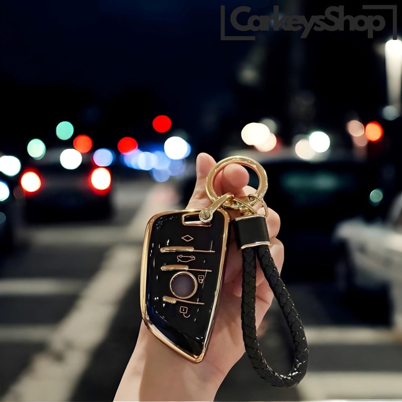 Pu&ograve; includere: Un portachiavi per auto nero e oro con un cinturino in pelle. Il portachiavi ha una forma di diamante e diversi pulsanti. Il cinturino &egrave; nero e intrecciato.