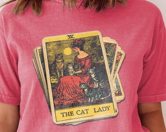 May include: A pink t-shirt with a vintage tarot card design featuring a woman with cats and the text "The Cat Lady".