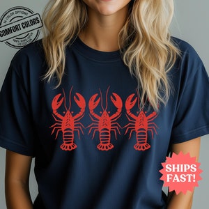 Comfort Colors T-shirt in navy featuring a bold red lobster graphic repeated across the chest, perfect for fisherman aesthetic and beach vibes.