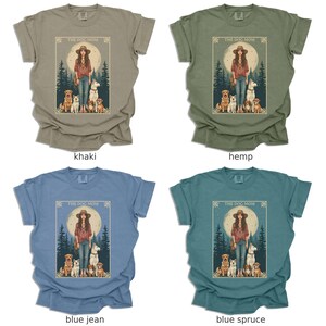May include: Four t-shirts in different colours, each featuring a graphic print of a woman with dogs in a woodland setting. The text "The Dog Mom" is printed on each shirt.