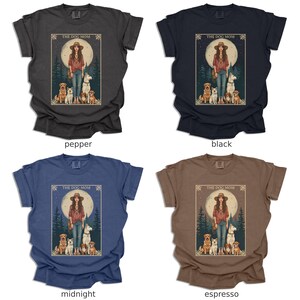 May include: Four t-shirts in different colours featuring a graphic design of a woman with four dogs in front of a full moon. The text "The Dog Mom" is above the image. The colours are pepper, black, midnight, and espresso.