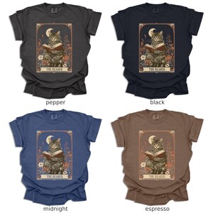 May include: Four t-shirts in different colours featuring a cat reading a book with a crescent moon above. The text on the t-shirt reads "The Reader". The colours of the t-shirts are pepper, black, midnight, and espresso.