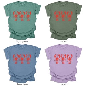 Puede incluir: Cuatro camisetas de diferentes colores: verde claro, musgo, azul vaquero y orqu&iacute;dea. Cada camiseta presenta un gr&aacute;fico de tres langostas rojas.