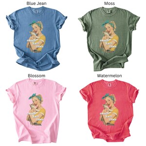 Puede incluir: Cuatro camisetas en azul vaquero, verde musgo, rosa flor y rojo sand&iacute;a. Cada camiseta presenta un gr&aacute;fico de estilo vintage de una mujer sosteniendo un gato, con el texto "me cat and I talk shit about you."