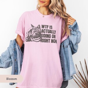 May include: A pink t-shirt with a black and white illustration of a cat and the text "WTF IS ACTUALLY GOING ON RIGHT NOW".