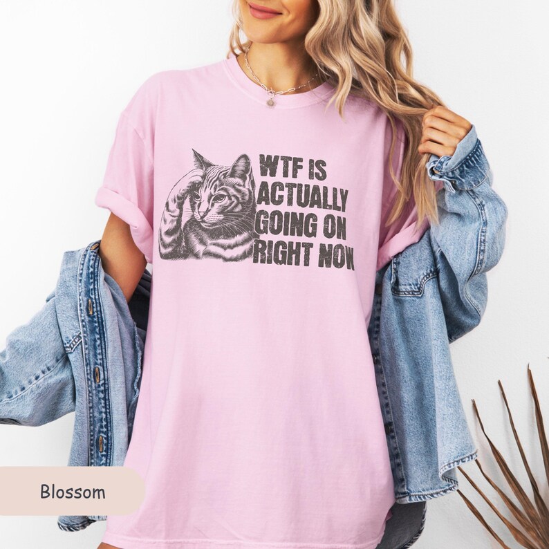 May include: A pink t-shirt with a black and white illustration of a cat and the text "WTF IS ACTUALLY GOING ON RIGHT NOW".