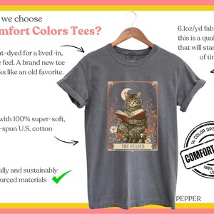 May include: A grey t-shirt featuring a vintage illustration of a cat reading a book. The illustration is surrounded by flowers and has the text "The Reader" at the bottom. The t-shirt is made from 100% ring-spun US cotton and is available in 14 colours.