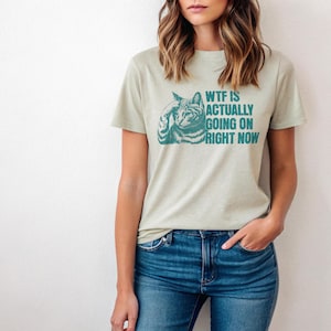 May include: A light green t-shirt with a teal cat graphic and the text "WTF IS ACTUALLY GOING ON RIGHT NOW".