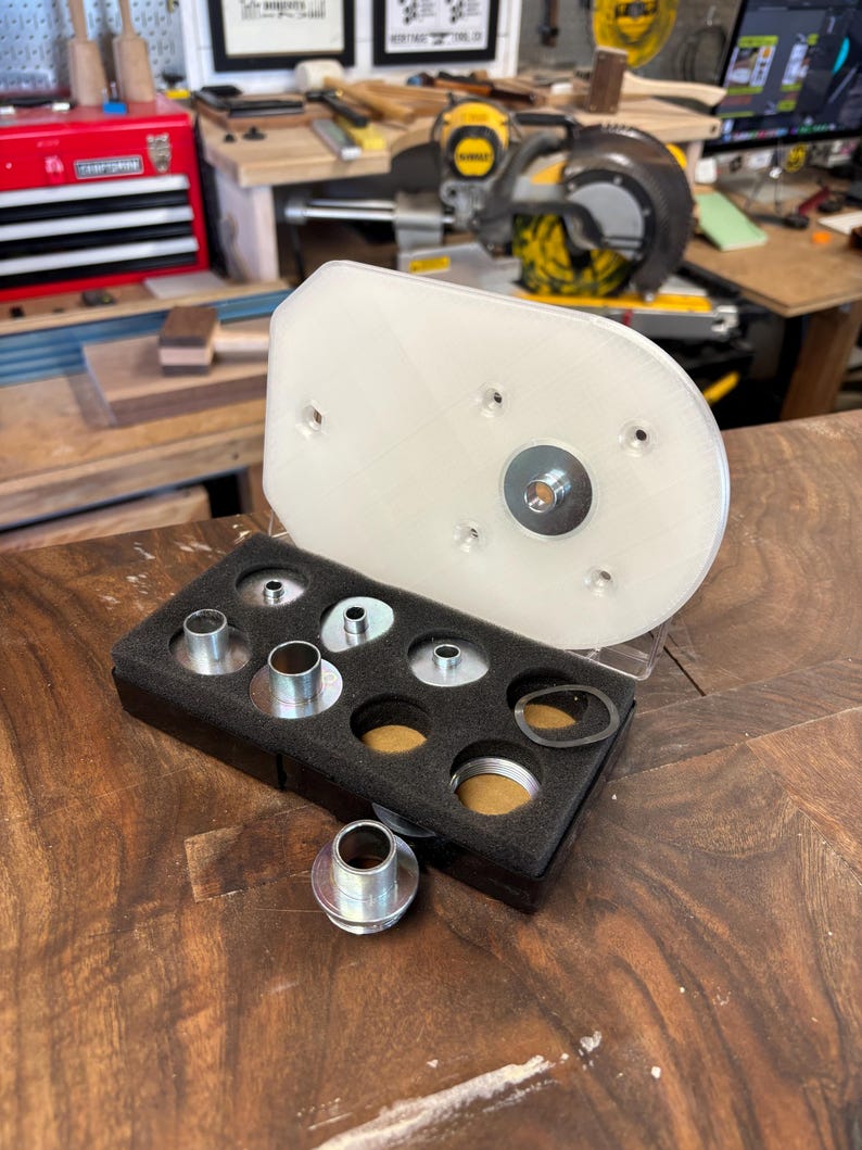 May include: A clear, rectangular router base plate with a metal insert and a set of metal bushings in a black foam insert. The items are for woodworking and are displayed on a wooden surface.