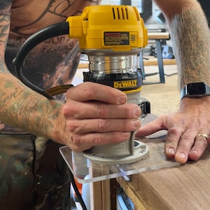 Puede incluir: Una persona usando una fresadora DeWalt amarilla y negra con una gu&iacute;a de pl&aacute;stico transparente para cortar una pieza de madera.