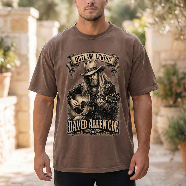May include: Brown t-shirt with a graphic of a man playing a guitar, the text reads "OUTLAW LEGION" and "DAVID ALLEN COE". The design is in a vintage style.