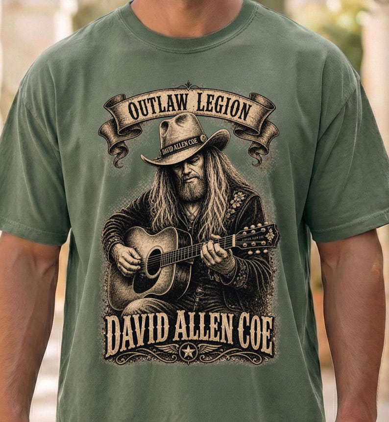 May include: Sage green t-shirt with a detailed graphic of a man with long hair and a cowboy hat playing an acoustic guitar. The shirt includes the text "OUTLAW LEGION" and "DAVID ALLEN COE" in a vintage style.