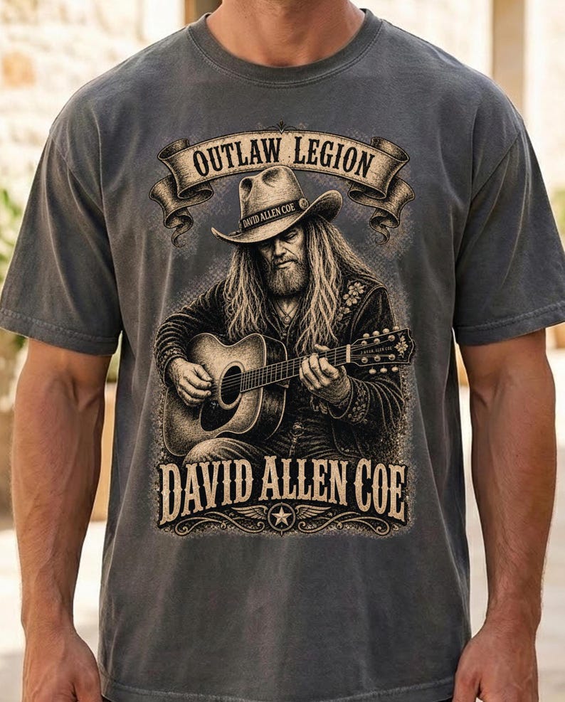 May include: Grey t-shirt with a graphic of a man playing a guitar, wearing a cowboy hat. The text reads "OUTLAW LEGION" above and "DAVID ALLEN COE" below the image, with a star emblem.