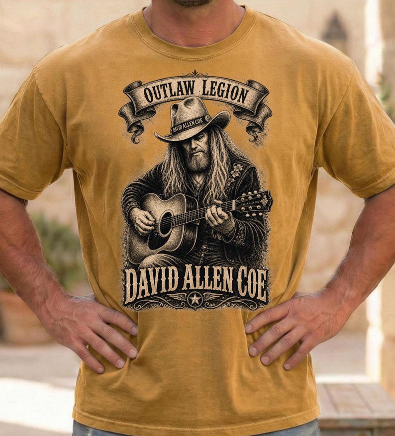 May include: Mustard yellow t-shirt with a graphic of a man playing a guitar, wearing a cowboy hat. The text "OUTLAW LEGION" is above the image, and "DAVID ALLEN COE" is below. The shirt has short sleeves.