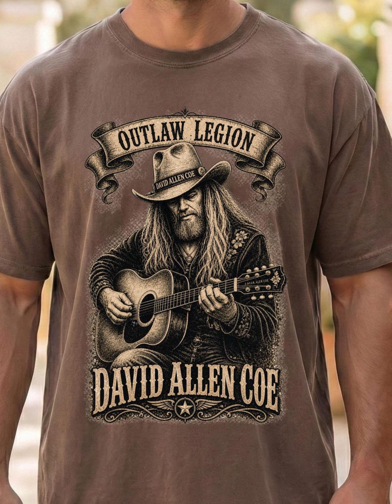 May include: Brown t-shirt with a detailed illustration of David Allen Coe playing a guitar. The design includes the text "OUTLAW LEGION" above and "DAVID ALLEN COE" below the image, with a star emblem.