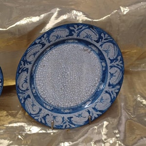 May include: Two white ceramic plates with blue floral designs around the rim. The plates have a crackled glaze finish.