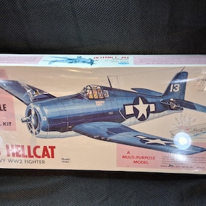 May include: A model kit box for a Grumman F6F-3 Hellcat U.S. Navy WW2 fighter plane. The box features a blue and white illustration of the aircraft with the number 13 on the tail and the text "Giant Scale Flying Model Kit".