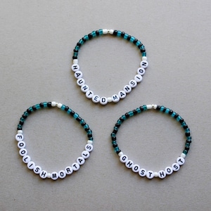 May include: Three beaded bracelets with black and teal beads. The bracelets spell out "Haunted Mansion", "Foolish Mortals", and "Ghost Host".