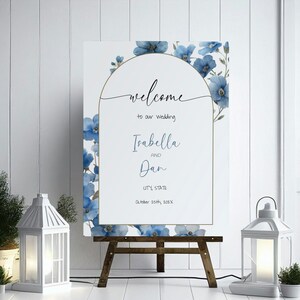 Puede incluir: Un cartel de bienvenida de boda con flores azules de acuarela y detalles dorados. El cartel dice "Bienvenido a nuestra boda Isabella y Dan [Ciudad, Estado] 25 de octubre de 202X".