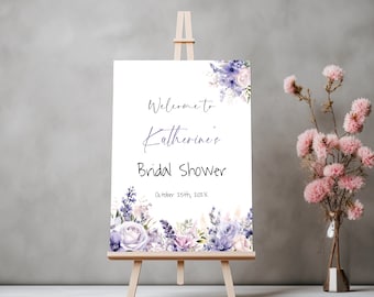 May include: A white sign with purple floral accents and the text "Welcome to Katherine's Bridal Shower, October 25th, 202X". The sign is on a wooden easel.